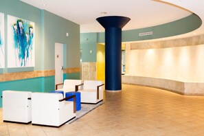 A lobby with a reception desk, white armchairs, a large blue pillar, and abstract art on the wall. - Beachfront| Free Beach Service| Majestic 5th floor-Pcb (Panama City Beach)