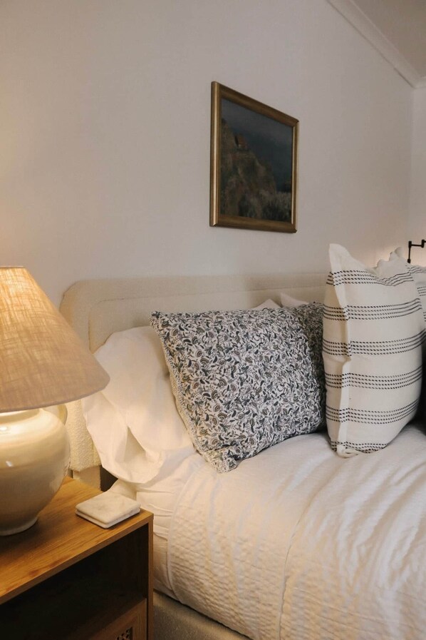 Un lit bien fait, agrémenté d’oreillers à motifs, une lampe de chevet et un tableau encadré au mur.