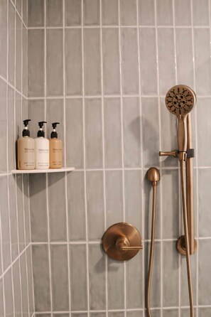 Ein Duschbereich mit einer goldfarbenen Duschbrause, zwei Handbrausen in Goldfarbe und einem Ablagebereich mit drei Flaschen Terra Pure Produkten.