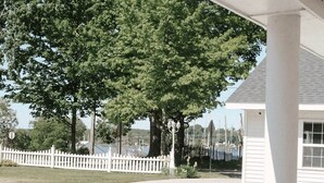 A covered outdoor area with a white fence, a large tree, and a building with a window. - The Lake Room - #12 (Whitehall)