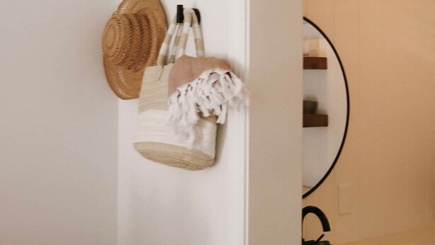 Une salle de bain avec un mur blanc, un miroir, un lavabo et un porte-serviettes agrémenté d’un panier en osier et d’une serviette blanche.