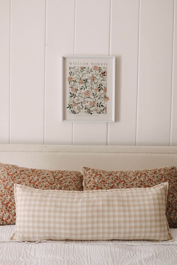 A bedroom with a bed, pillows, and a framed picture on the wall.