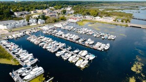 Vue aérienne d’une marina où de nombreux bateaux sont amarrés selon un plan bien défini, le tout étant entouré de bâtiments et de verdure.