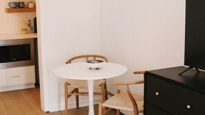 Un espace de vie compact comprenant une table ronde blanche, des chaises en bois, un meuble noir et un coin cuisine équipé d’un four à micro-ondes et d’étagères.
