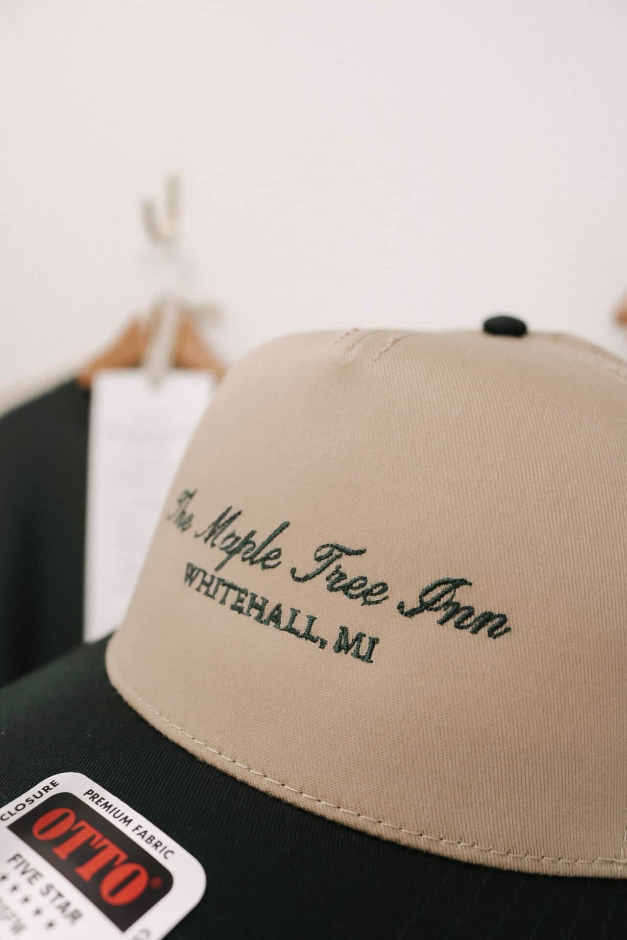 Une casquette de baseball ornée d’un texte brodé : « The Maple Tree Inn, Whitehall, MI », et d’une étiquette indiquant « Tissu de qualité supérieure, cinq étoiles ».