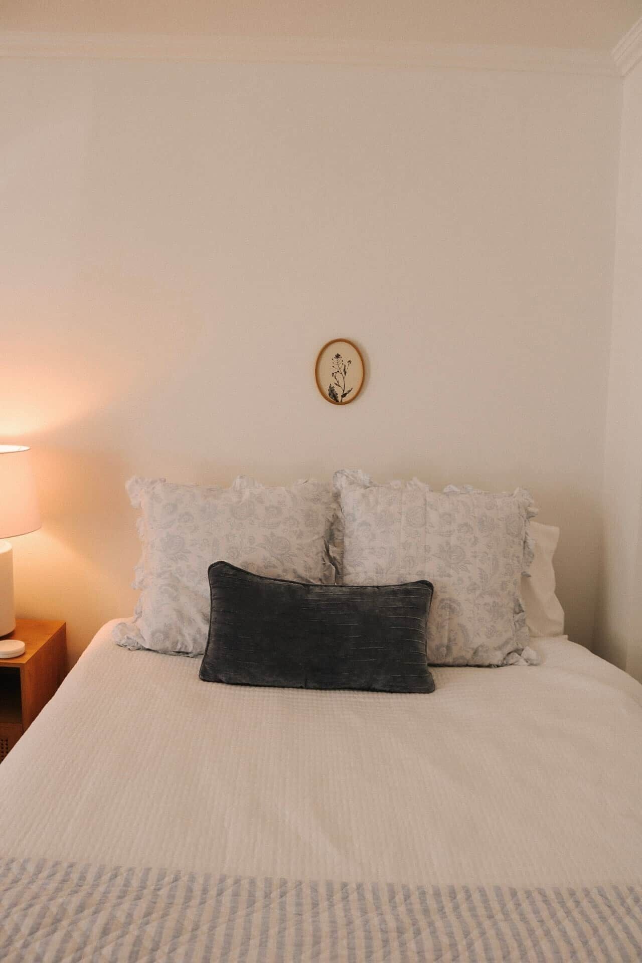 A bed with white bedding, a dark pillow, and a wall-mounted picture.