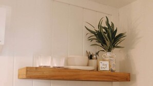 Trois étagères en bois, sur lesquelles sont disposés divers ustensiles de cuisine, une plante en pot et une machine à café.