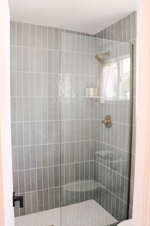 A shower with a glass door, a towel rack, and a small shelf with toiletries.