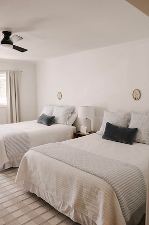 Two single beds with white bedding, a ceiling fan, a bedside table with a lamp, and a window with curtains. - The Sky Room - #16 (Whitehall)