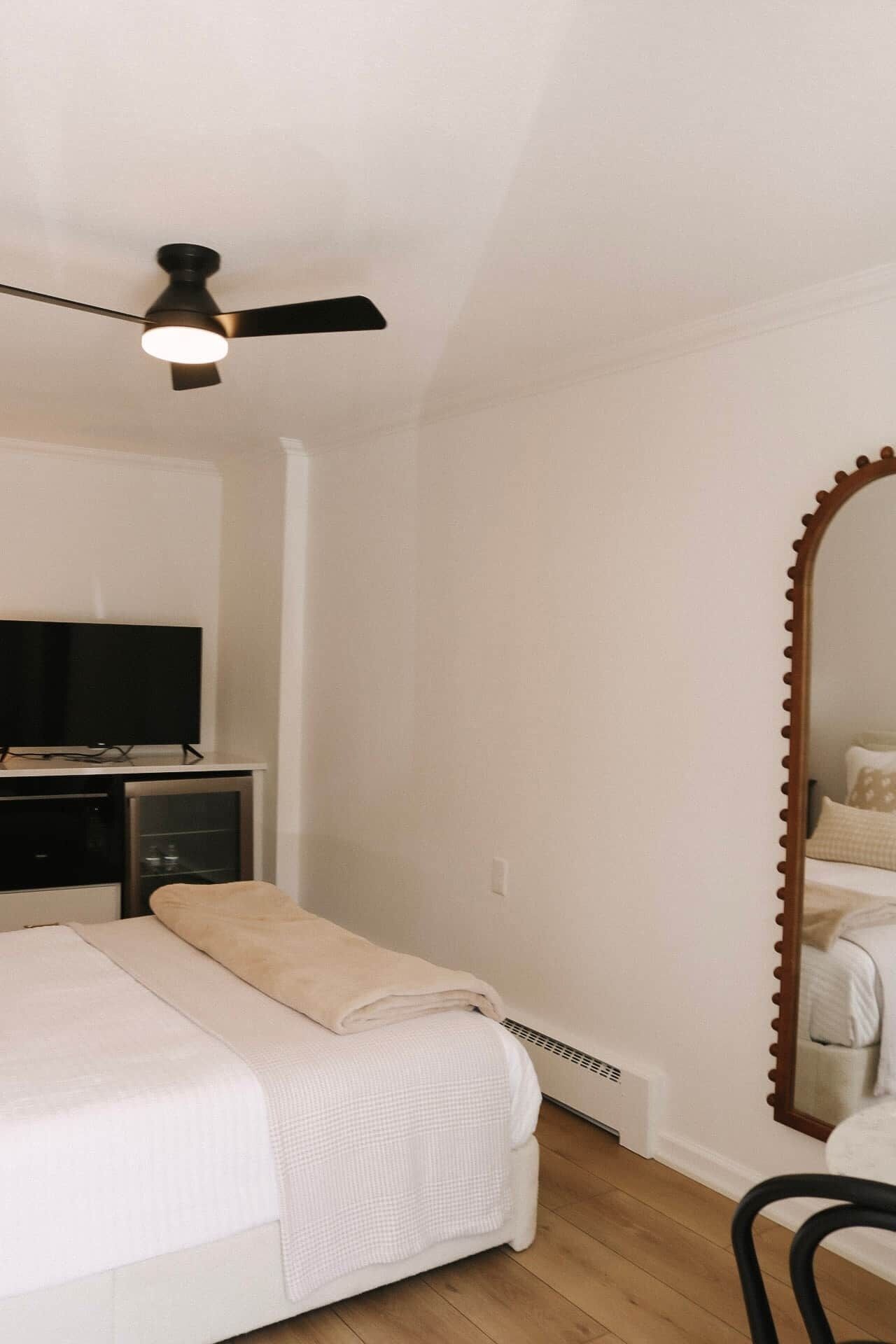 A bedroom with a bed, a ceiling fan, a TV, and a mirror.