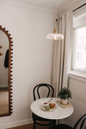 Een eetruimte met een ronde tafel, stoelen, een hanglamp, een spiegel en een raam met gordijnen.