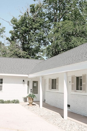 A white building with a covered porch, a door, and a window with shutters. - The Dune Room -  #17 (Whitehall)