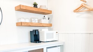 A compact kitchenette with a coffee maker, microwave, and mini-fridge. There are wooden stools and a wooden hanger rack. - The Midnight Room - #22 (Whitehall)