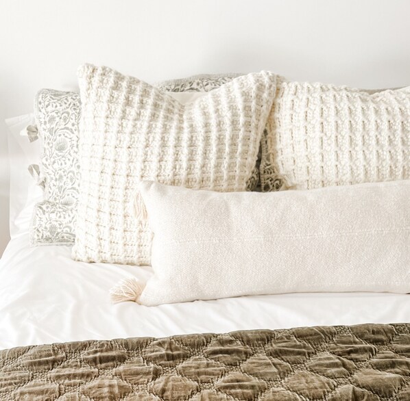A bed with white bedding and a brown quilt.