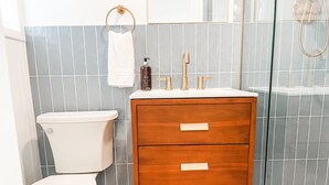 Une salle de bain avec des toilettes blanches, un meuble-lavabo en bois doté de deux tiroirs, un miroir et un espace douche.