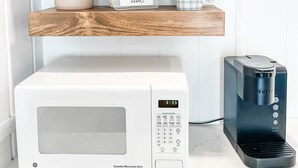 Une cuisine équipée d’un four à micro-ondes GE, d’une machine à café Keurig et d’étagères en bois où sont rangés les ustensiles de cuisine et une plante.