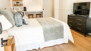 Une chambre à coucher avec un lit, des tables de chevet, une commode, un téléviseur et, au fond, un coin cuisine.