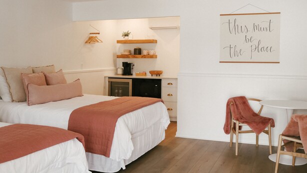 Een slaapkamer met twee bedden, een kleine kitchenette, een plafondventilator en een bord op de muur.