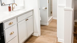 Een badkamer met witte kastjes, een grote spiegel en een wastafel met gouden details.