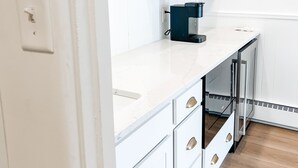 A modern kitchen with white cabinetry, wooden shelves, and a coffee machine. - The Goldie Room - #21 (Whitehall)