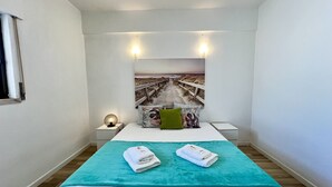 Een slaapkamer met een bed, een hoofdbord met een strandafbeelding, twee bedlampen en een raam met gordijnen.