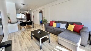 Een moderne woonkamer met een grijze bank, een zwarte salontafel en een eethoek met een zwarte tafel en stoelen.