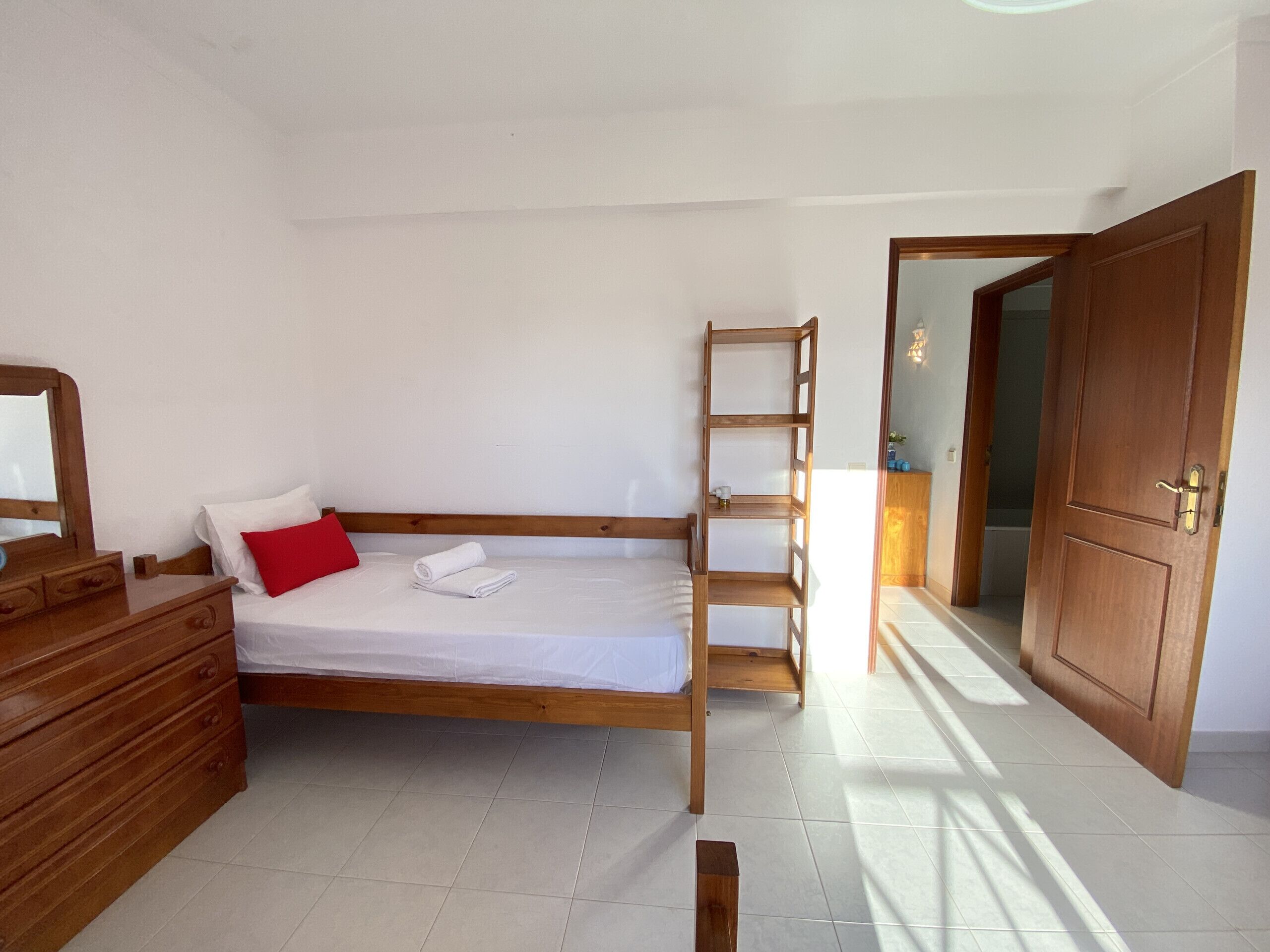 Ein Schlafzimmer mit einem hölzernen Bett, einer hölzernen Kommode, einem roten Kissen, einem weißen Handtuch und einer Holzleiter.