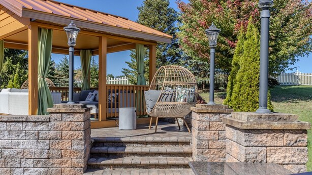 A covered outdoor seating area with stone steps leading up to a wooden deck, wicker chairs, and a birdcage. - VellaVue Luxury Estate: Private Indoor Pool, Sauna, Gym & Theater – Sleeps 20 (Friendsville)