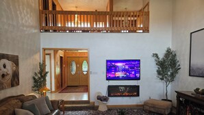A living room with a leather sofa, a glass coffee table, a flat-screen TV, a fireplace, and a staircase leading to an upper level. - VellaVue Luxury Estate: Private Indoor Pool, Sauna, Gym & Theater – Sleeps 20 (Friendsville)