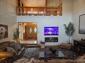 A living room with a leather sofa, a glass coffee table, a flat-screen TV, a fireplace, and a staircase leading to an upper level.