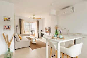 A modern living room with a white sofa, a dining table with chairs, a ceiling fan, and a fireplace. - Modern Penthouse w/Rooftop Terrace, Parking + Lift, 360 Views + Optional Hot Tub (Cómpeta)