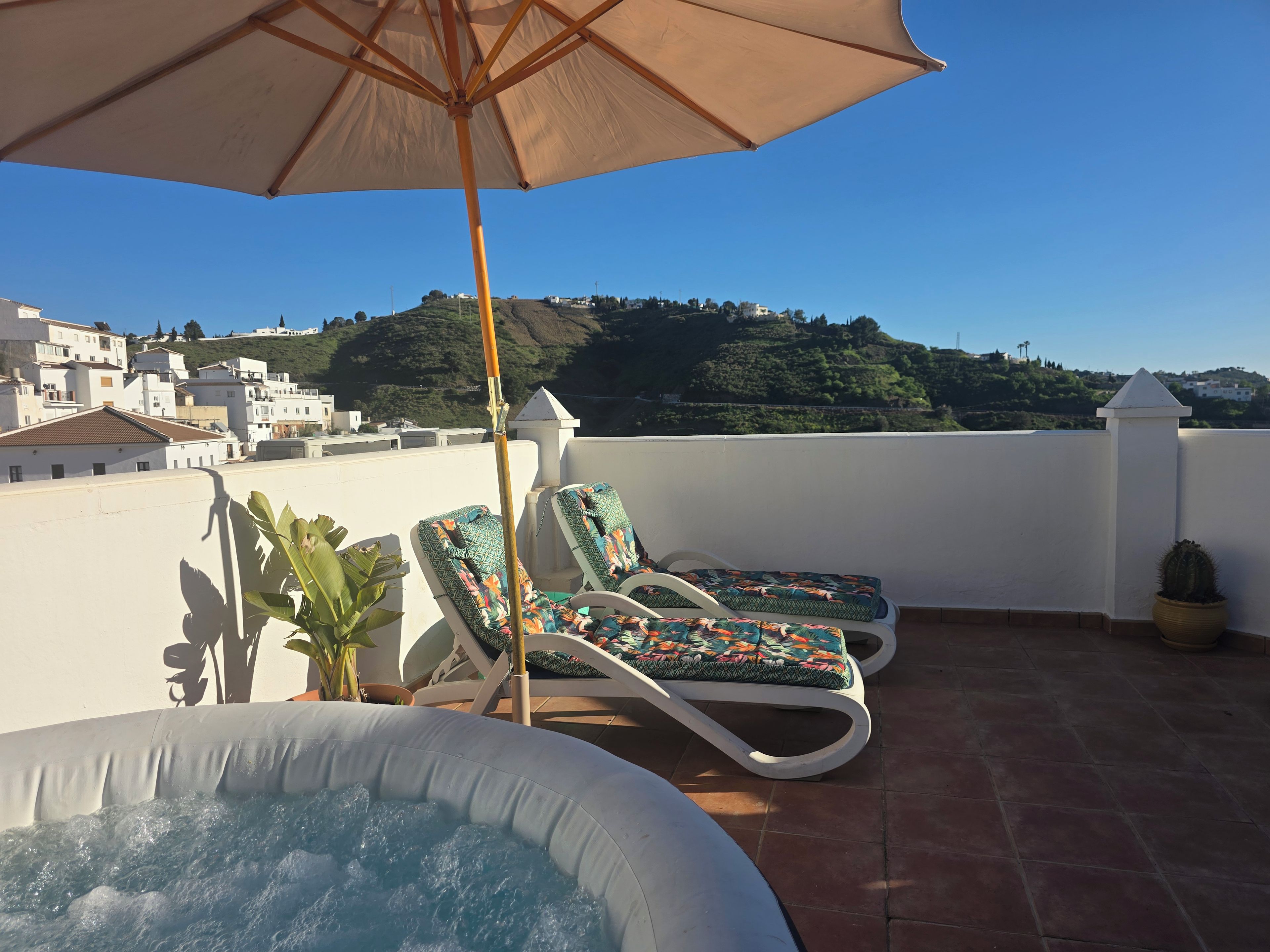 A rooftop terrace with a hot tub, lounge chairs, and an umbrella.