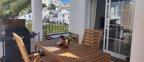 A balcony with a wooden table, chairs, a grill, and a potted plant.
