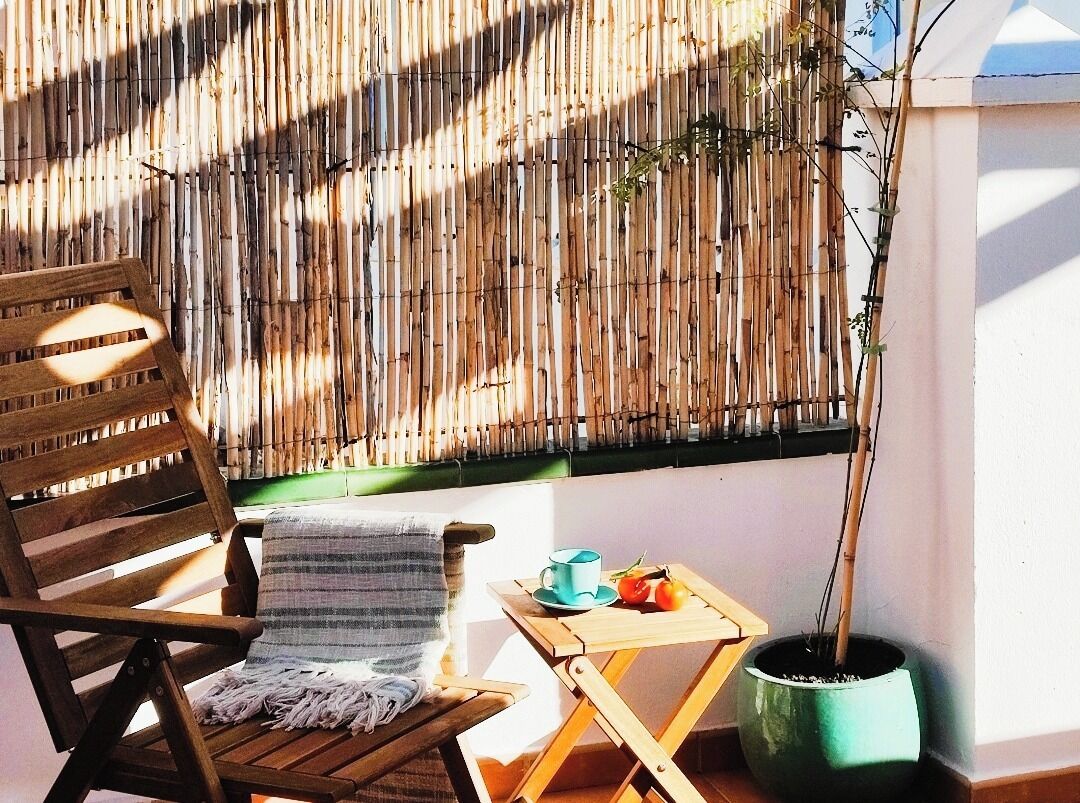 A wooden chair with a striped blanket, a small table with a cup and fruit, and a potted plant.