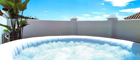 An outdoor hot tub surrounded by a white wall and a clear blue sky.
