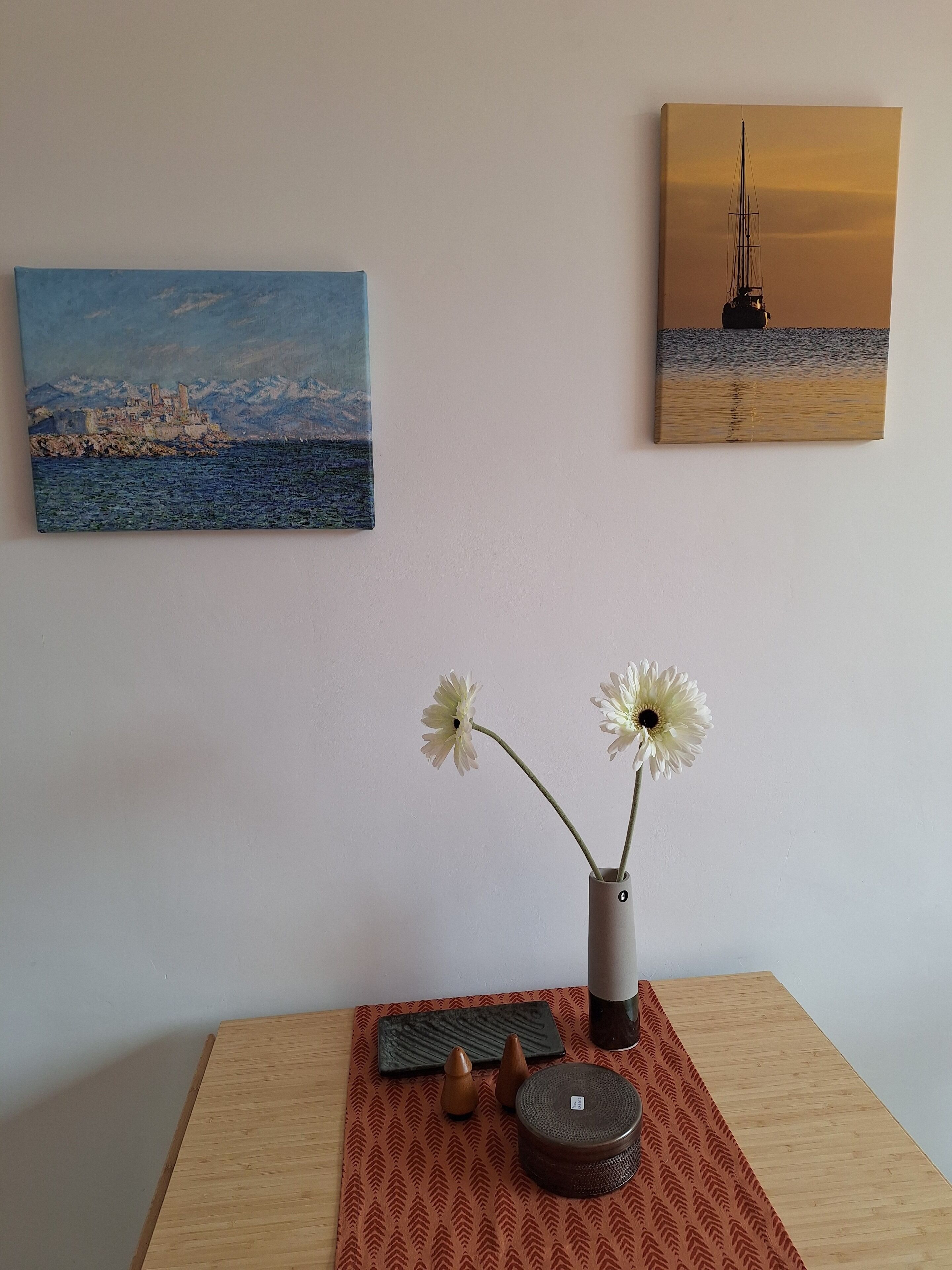 A room with a wooden table, a vase with flowers, and two paintings on the wall.