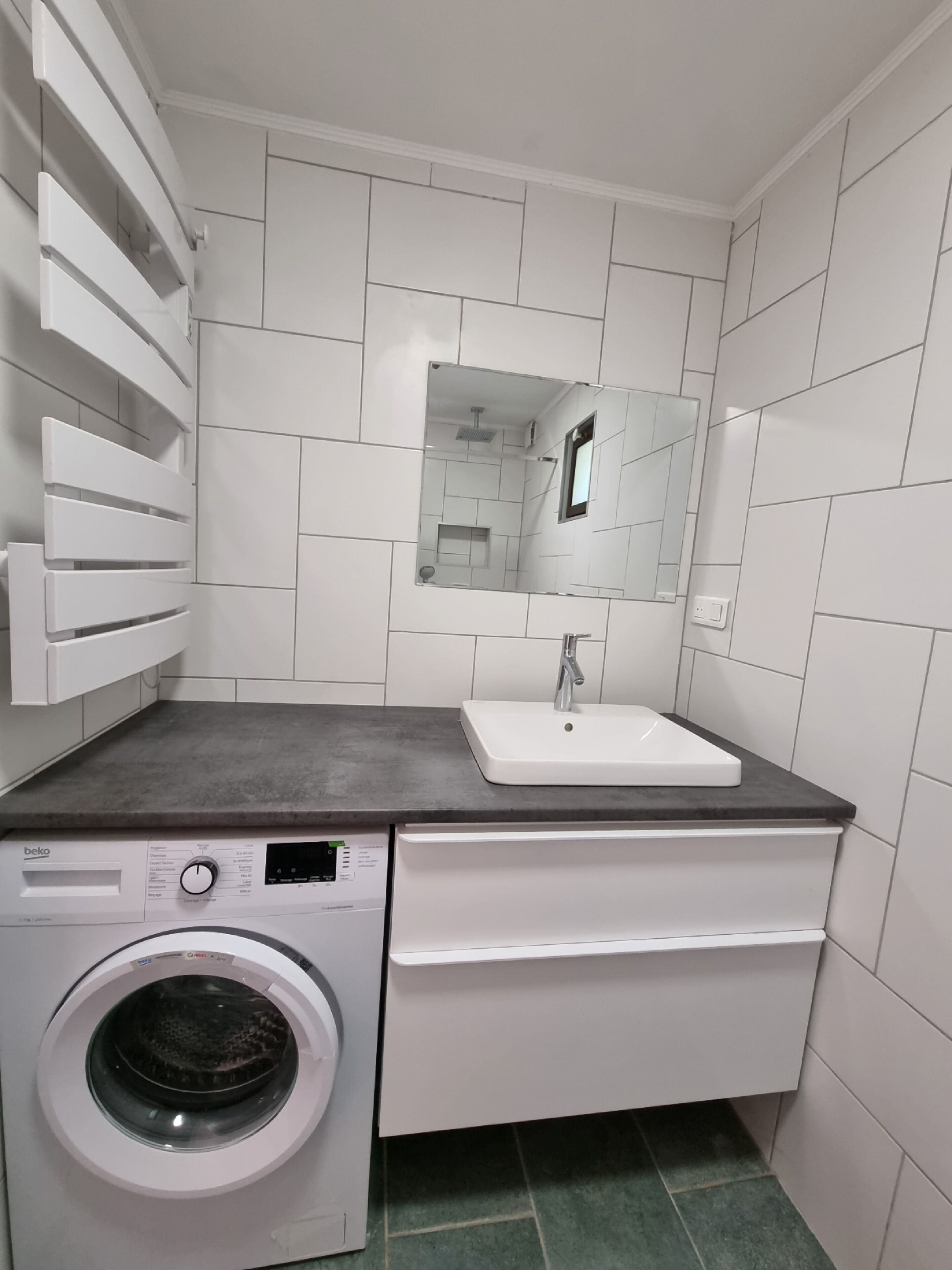 A compact laundry room with a washing machine, a sink, and a mirror.