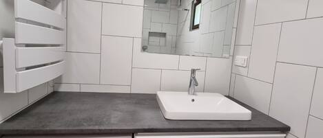 A compact laundry room with a washing machine, a sink, and a mirror.