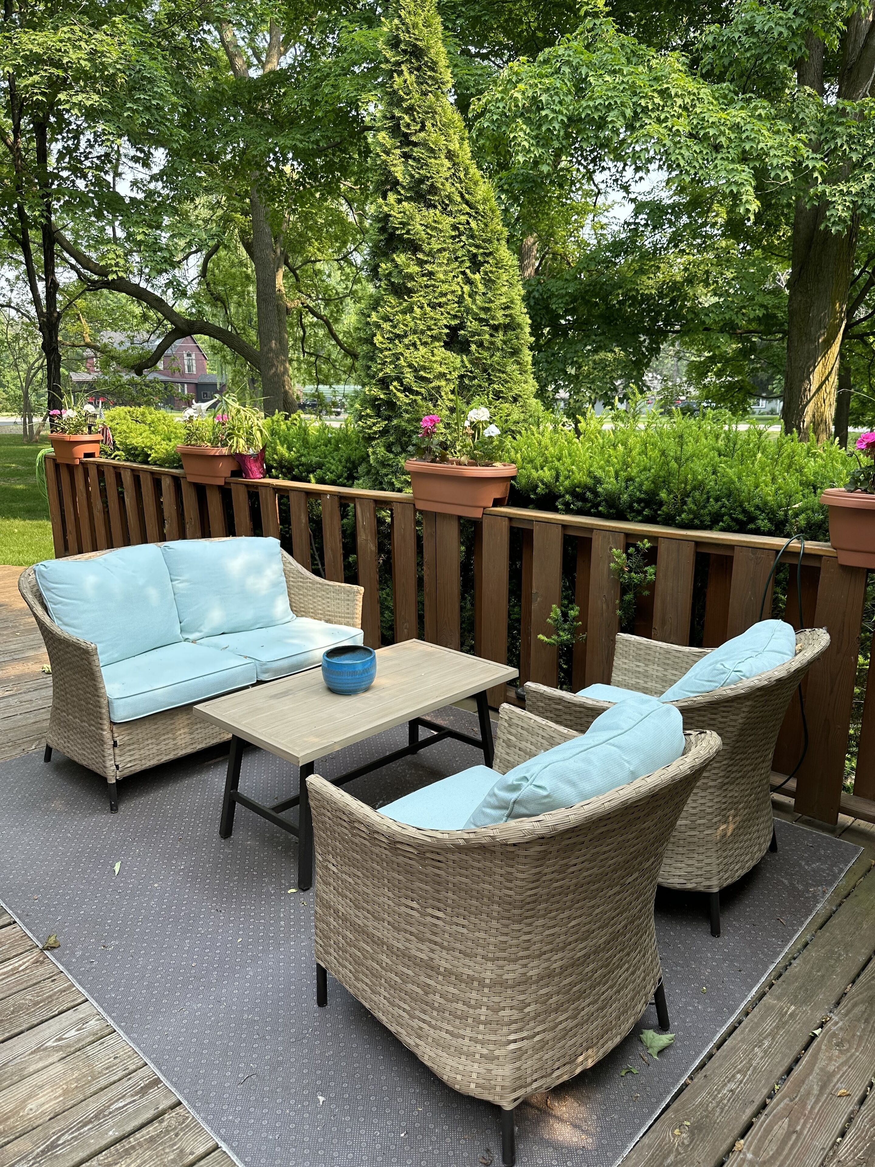 A patio with wicker furniture, a wooden table, and potted plants.