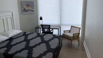 Quarto com uma cama, uma cadeira, uma mesa pequena e uma janela com persianas.