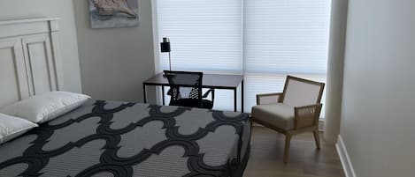 Ein Schlafzimmer mit Bett, Sessel, Nachttisch und einem Fenster mit Jalousien.