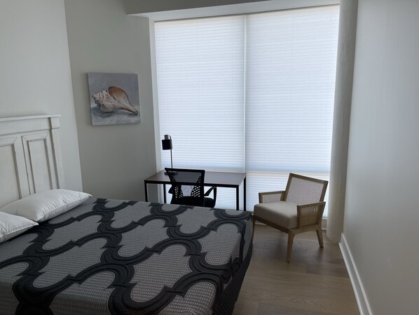 Une chambre à coucher avec un lit, une chaise, une petite table et une fenêtre avec des stores.