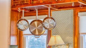 Une cuisine avec des casseroles suspendues, un mur en briques, une fenêtre et une lampe.