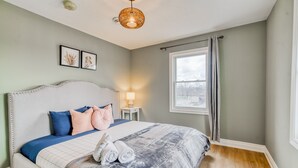 Une chambre à coucher bien rangée, avec un grand lit, une lampe de chevet et des illustrations botaniques encadrées accrochées au mur.
