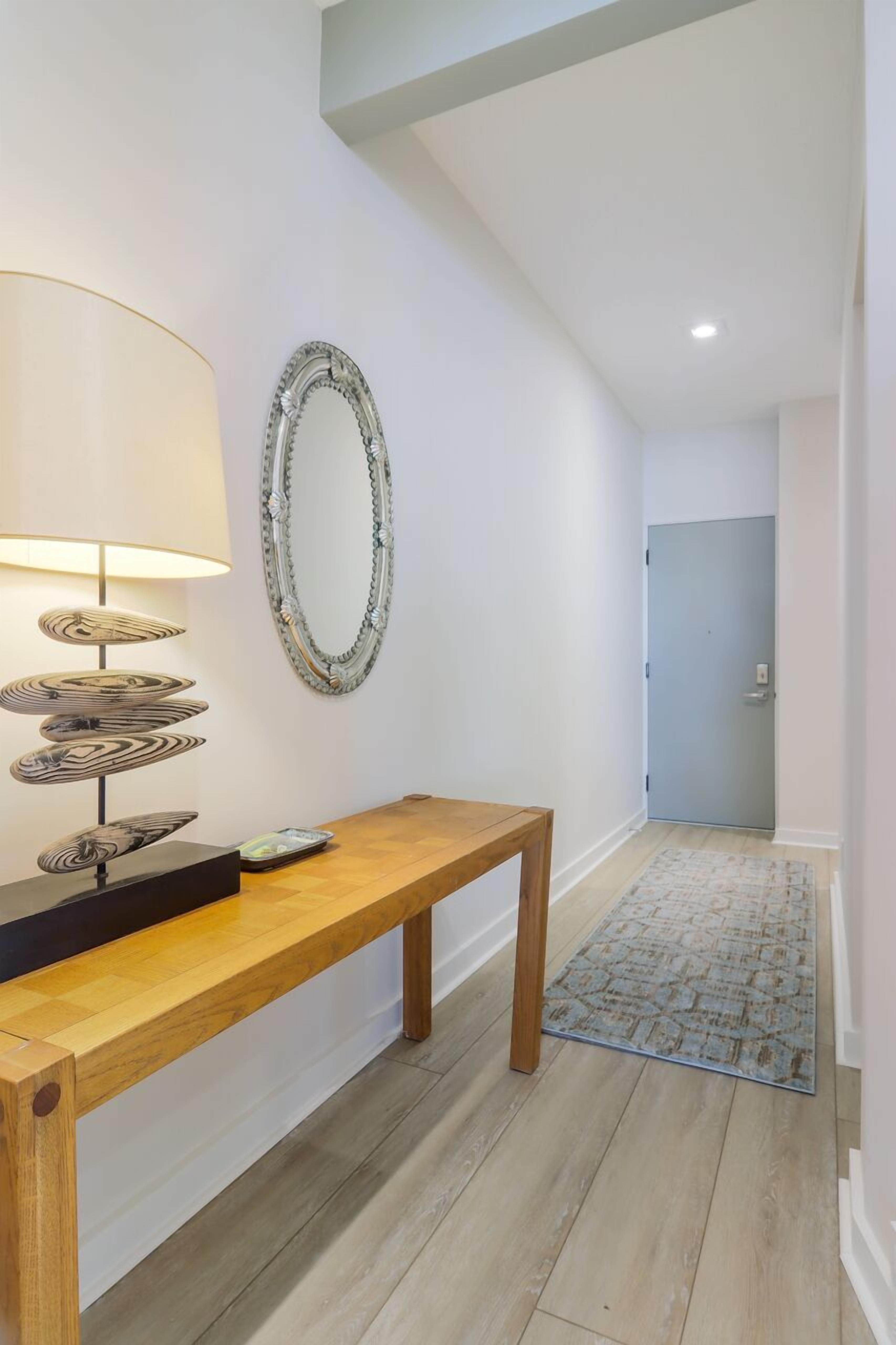 Un couloir avec un banc en bois, un miroir fixé au mur et un tapis à motifs.