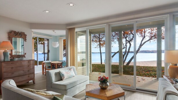 Una sala de estar moderna con un gran ventanal corredizo que da a una terraza con vista a un lago.