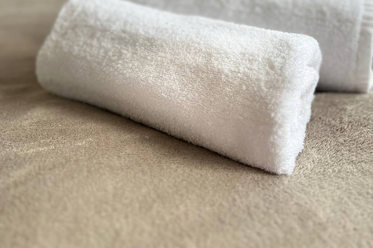 A neatly made bed with two white towels folded at the foot.