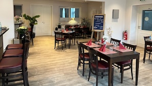 Un restaurant avec des tables et des chaises en bois, un menu écrit à la craie et des plantes en pot.