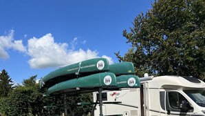 Un camping-car blanc, équipé d’une remorque à plateau, transportait trois kayaks verts.