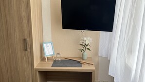 Une pièce comprenant un bureau en bois, un téléviseur fixé au mur, un vase avec des fleurs et une armoire.